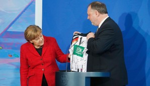 Als Gast-Geschenk überreicht DHB-Präsident Andreas Michelmann der Kanzlerin ein von allen Spielern signiertes Deutschland-Trikot mit der Nummer eins auf dem Rücken und dem Schriftzug Merkel